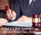 There is an unseen man in a business attire holding up a pen over an important document. There is also another person off-camera preparing to write something on it. There is a gavel and scales of justice beside the man. The title of the article, "What a CRM System Can Do for Your Law Firm," is written below.